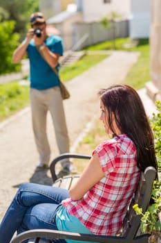 Young man take photo of his girlfriend sitting park bench