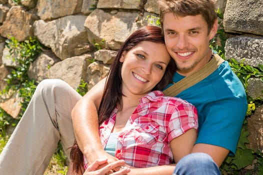Young couple in love sitting leaning against wall sunny day