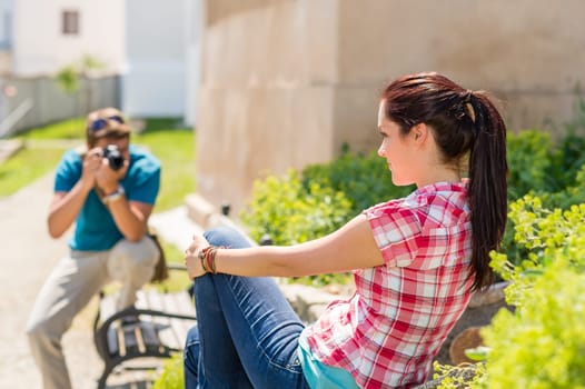 Young man take photo of his girlfriend sitting park bench