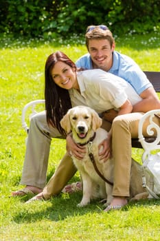 Happy young couple sitting with golden retriever dog in park