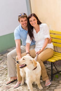 Young smiling couple with dog sitting on yellow bench