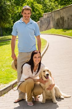 Happy young couple with dog posing on sunny park alley