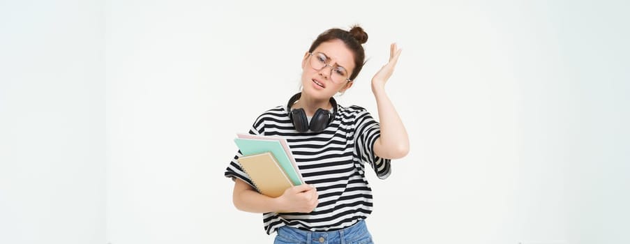 Image of upset young woman, student in glasses complains at difficult task at university, holding notebooks, forgot to do something, white background.