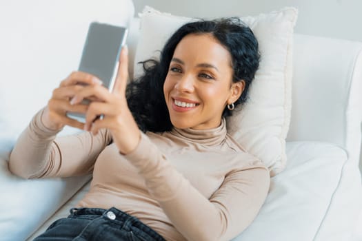 Relaxed young African American woman using crucial mobile phone on sofa couch in living room at home