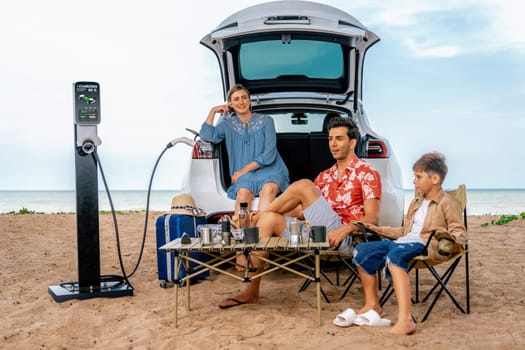 Family vacation trip traveling by the beach with electric car, happy family recharge EV car, enjoying outdoor camping coffee. Seascape travel and eco-friendly car for clean environment. Perpetual