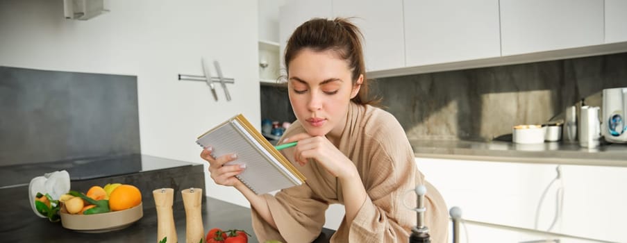 Portrait of modern young woman cooking, making grocery list, reading recipe and making meal, salad in the kitchen, looking at vegetables on chopping board.