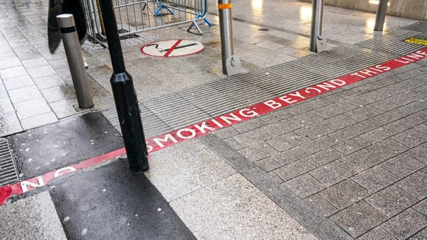 Red line on pavement with NO SMOKING text, sign near also informing pedestrians they're entering non-smoking area.