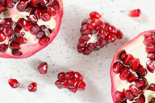 Tabletop closeup view - pomegranate half, clusters of gem like fruits scattered on white board.