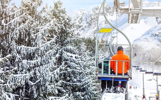 Skiers on chair lift, piste under, snow covered trees on right side