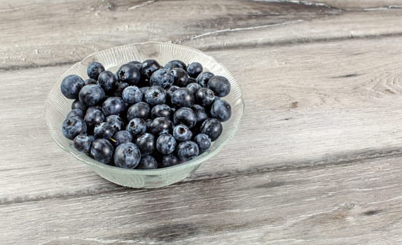 Small glass bowl with blueberries on gray wood desk.