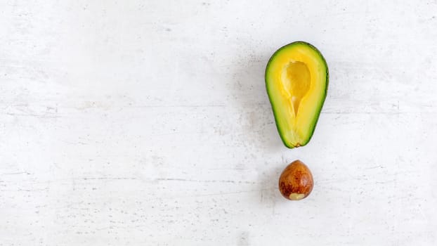 Exclamation mark made of avocado half and seed, on white board, photo from above. Wide banner with space for text on left side.