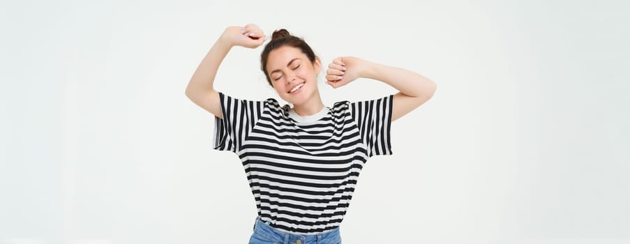 Portrait of woman feeling pleased after good nap, stretching arms and smiling, standing over white background.