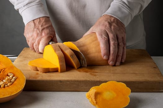 Caucasian unrecognizable middle-aged man cutting pumpkin on a wooden cutting board. Selective focus.