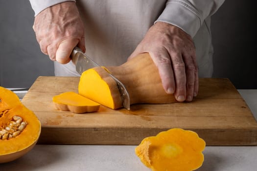 Caucasian unrecognizable middle-aged man cutting pumpkin on a wooden cutting board. Selective focus.