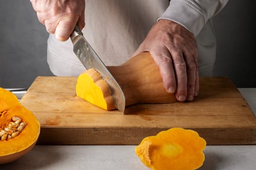 Caucasian unrecognizable middle-aged man cutting pumpkin on a wooden cutting board. Selective focus.