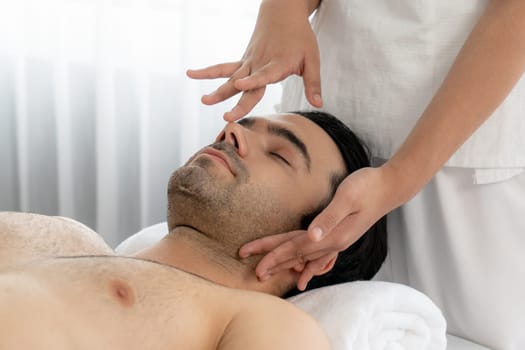 Caucasian man enjoying relaxing anti-stress head massage and pampering facial beauty skin recreation leisure in dayspa modern light ambient at luxury resort or hotel spa salon. Quiescent