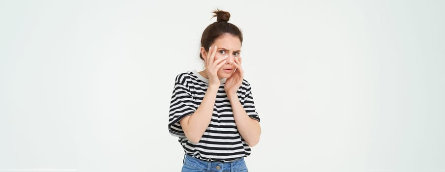 Image of woman looking scared, apalled by something shocking, standing over white background.