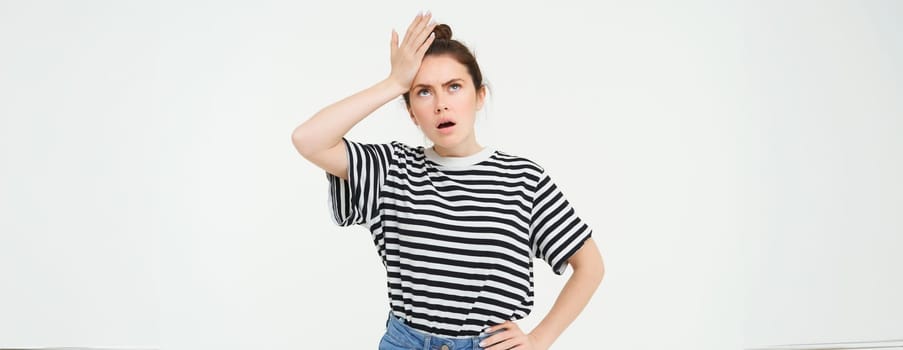Portrait of shocked woman facepalm, slaps her forehead and looks upset, stands over white background.
