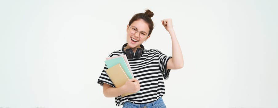 Enthusiastic young woman in glasses, teacher celebrating, raising hand up and cheering, tirumphing with joyful smile, white background.