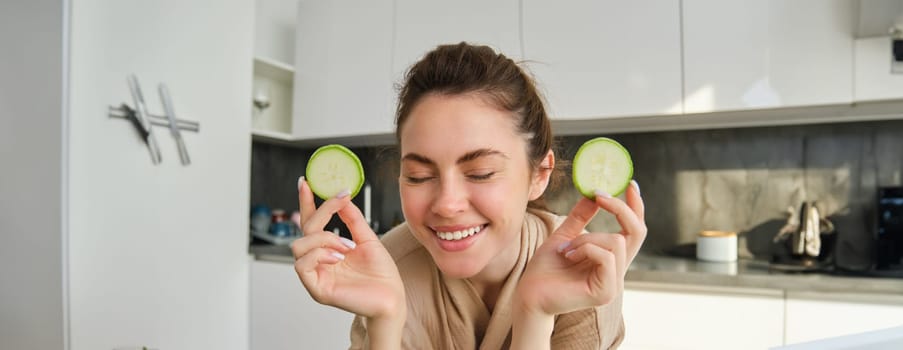 Portrait of happy, smiling young woman in the kitchen, cooking, chopping zucchini, holding vegetables and looking happy, preparing vegan food meal at home.