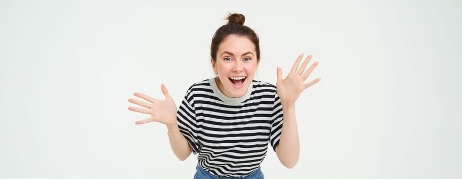 Portrait of happy, beautiful girl makes jazz hands, tells big news, revelation, introduces surprise, stands over white background.