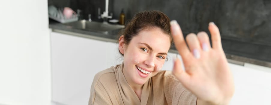 Attractive young cheerful girl baking at the kitchen, making dough, holding recipe book, having ideas.