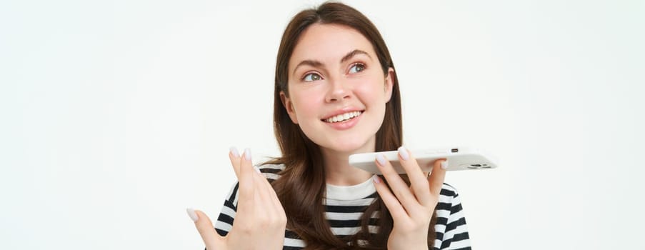 Portrait of happy young woman, student recording voice message, holding smartphone near lips, talking into mobile phone speakerphone, explaining something, singing, translating her words.