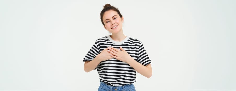 Portrait of smiling modern woman, holding hands on heart, says thank you, expresses her warm feelings, white background.