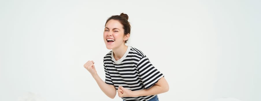 Portrait of happy woman winning, celebrating victory, rooting for team, triumphing, standing over white background.