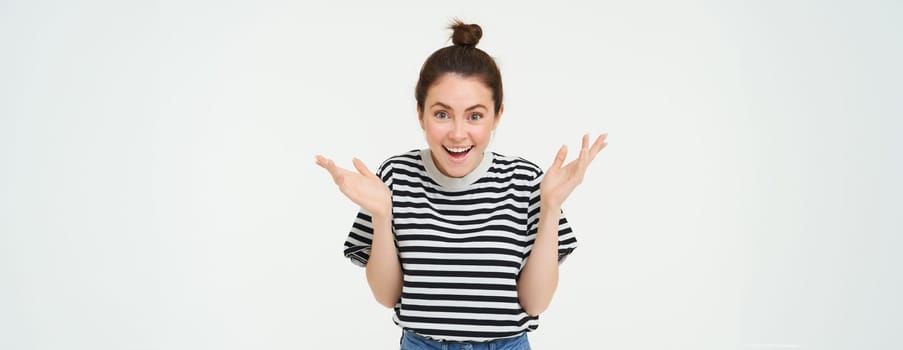 Image of happy woman hear great news, looking surprised, claps hands and smiling, isolated against white background.