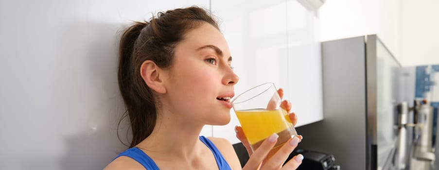Beautiful woman drinking an organic orange juice. Fit young woman drinking from glass. Healthy girl enjoy detox drink and looking away.