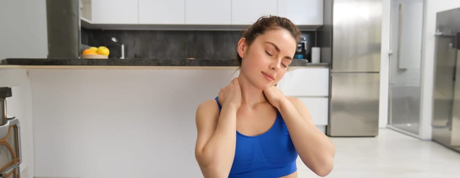 Portrait of woman workout from home, does training exercises, stretches her neck, warm-up before fitness. Sport and wellbeing concept