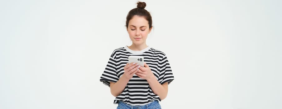 Technology and lifestyle. Young woman standing over white background with smartphone.