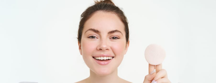 Wellbeing and skin care concept. Beauty woman shows cotton pad after washing her face with cleanser, using toner to take off makeup, standing over white background.