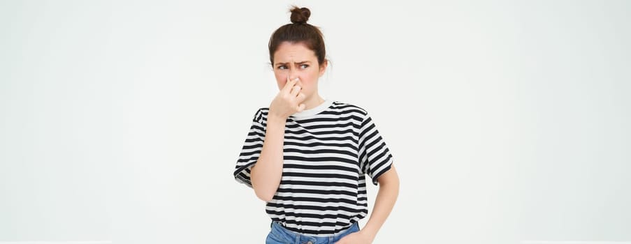 Young woman shuts her nose with fingers from disgusting smell, isolated on white background.