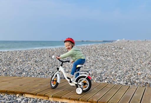 3 Years old Girl in helmet learns riding a four-wheeled bicycle nea sea