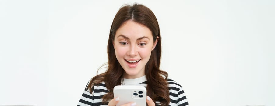 Portrait of young woman looking at smartphone screen with surprised, amazed face expression, reading great news on phone.