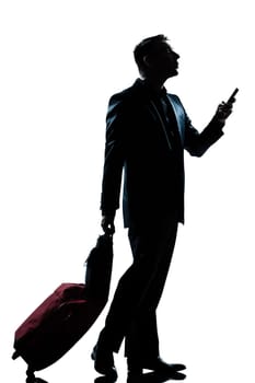 one caucasian business traveler man walking on the phone with suitcase  full length silhouette in studio isolated white background
