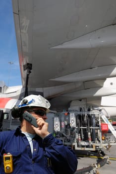 airplane-mechanic, working and re-fuelling a commercial airplane, standing under the wing of aircraft