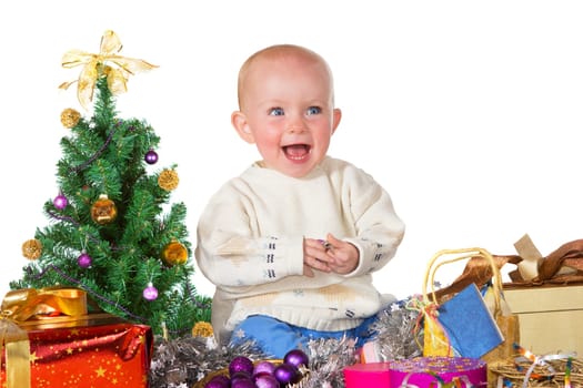 Adorable laughing baby sitting on the floor surrounded by a Christmas tree, gifts and decorations