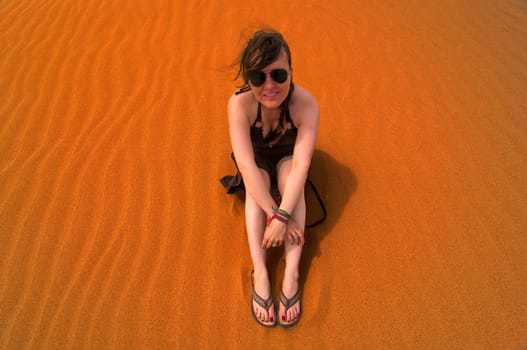 Caucasian woman sitting in sand on top of a sand dune.