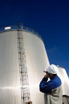 oil woorker, engineer with giant sunlit fuel storage tower in background