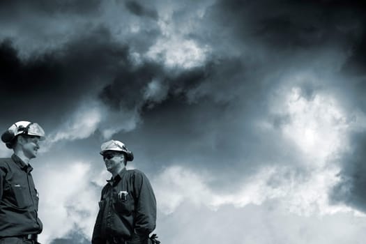 two engineers, workers, standing under a dark toxic cloud-scape, conceptual image