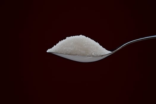 Pile of sugar on chromed spoon on background