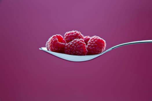 Fresh raspberry on metal chromed spoon on background