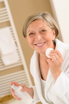 Senior woman clean face with cotton pad looking at camera