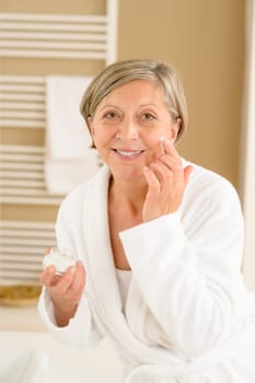 Senior woman hold anti-wrinkles cream in bathroom looking at camera
