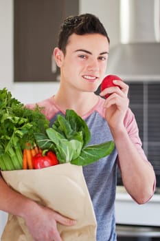 Handsome young man holding a bag of organic groceries eating a red apple
