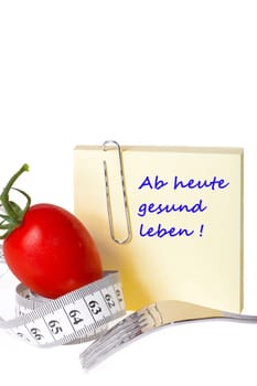 Sticky note with inscription: From today healthy living - Yellow notepad with the inscription: From today healthy living with paper clip behind a tomato with measuring tape and a fork against a white background