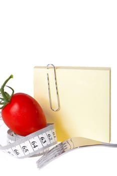 Blank notepad - Healthy eating - Yellow blank notepad with paper clip behind a tomato with tape measure and fork against white background